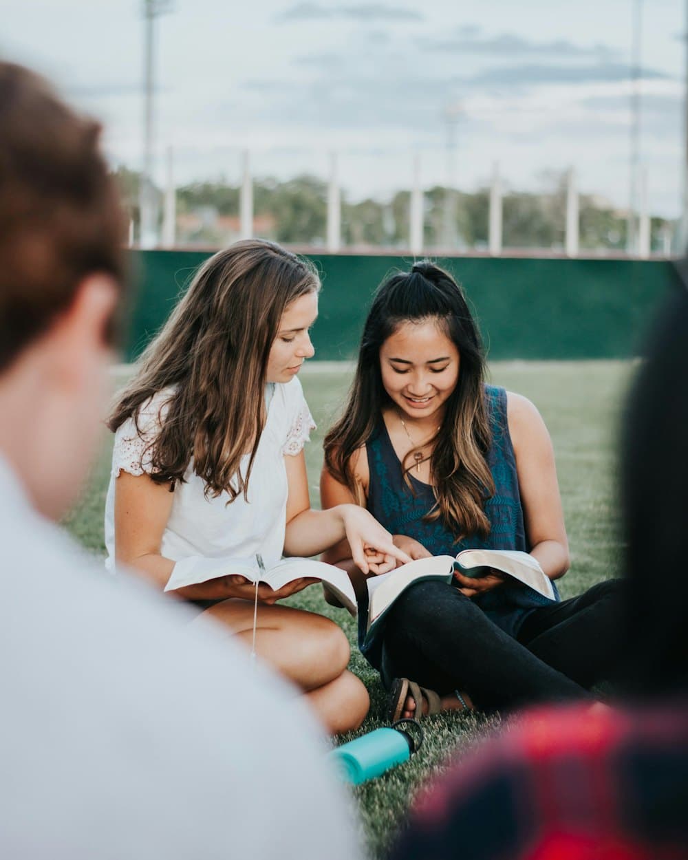 Three students sitting on the grass, reading together.