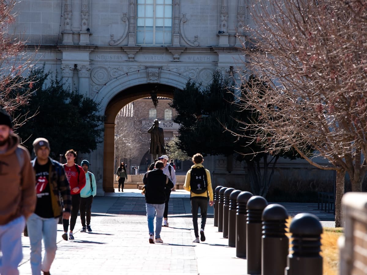 Students walking through a university archway on a bright winter day.
